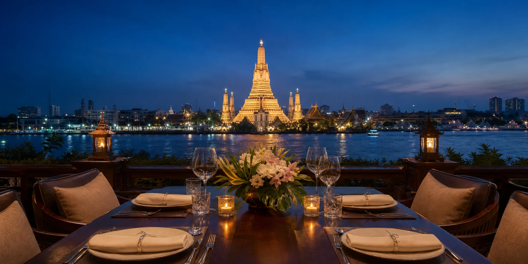 Riverside dining table overlooking illuminated Wat Arun in Bangkok at night.