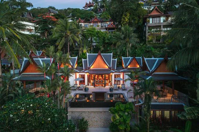 Front-facing Thai villa surrounded by palms and lush hillside greenery.